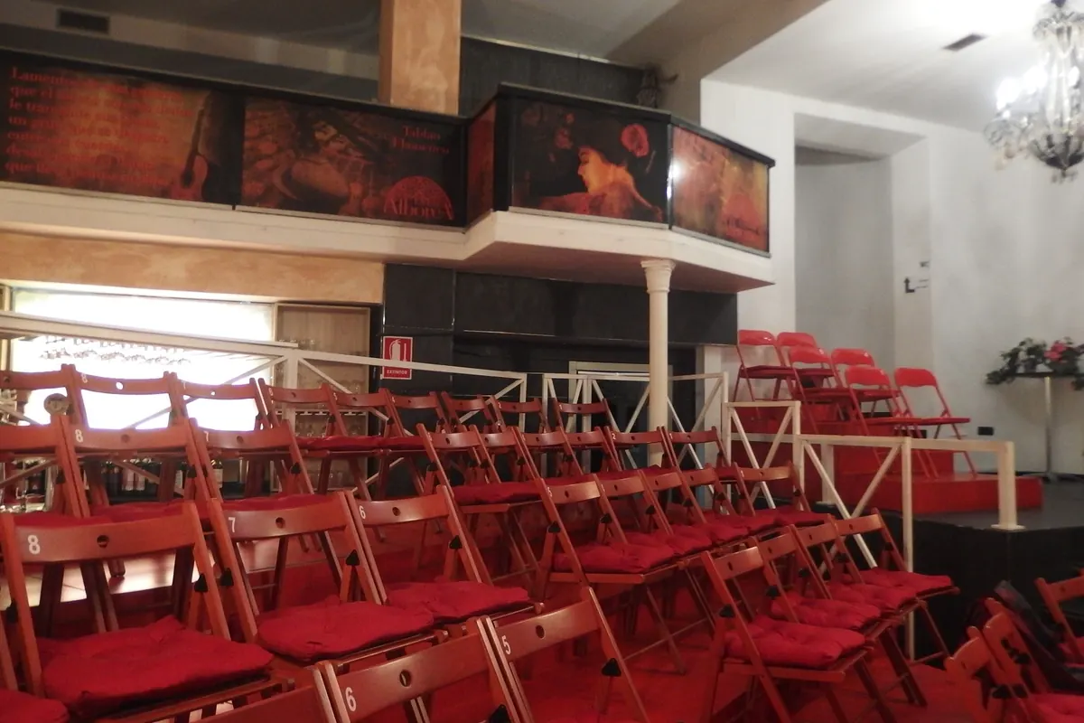 Rows of numbered wooden chairs with red cushions face a low stage at La Alboreá, with a mezzanine above