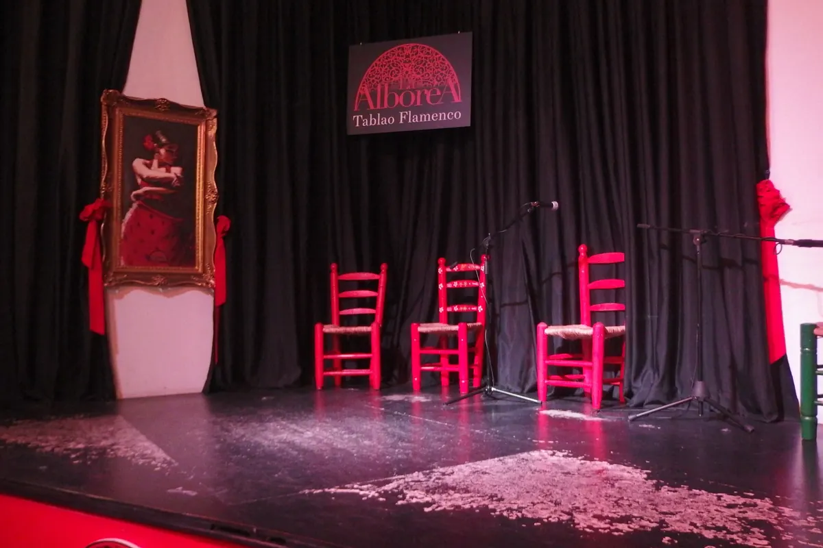 The empty stage of La Alboreá with red rush-seated chairs, a framed painting of a dancer and the venue sign